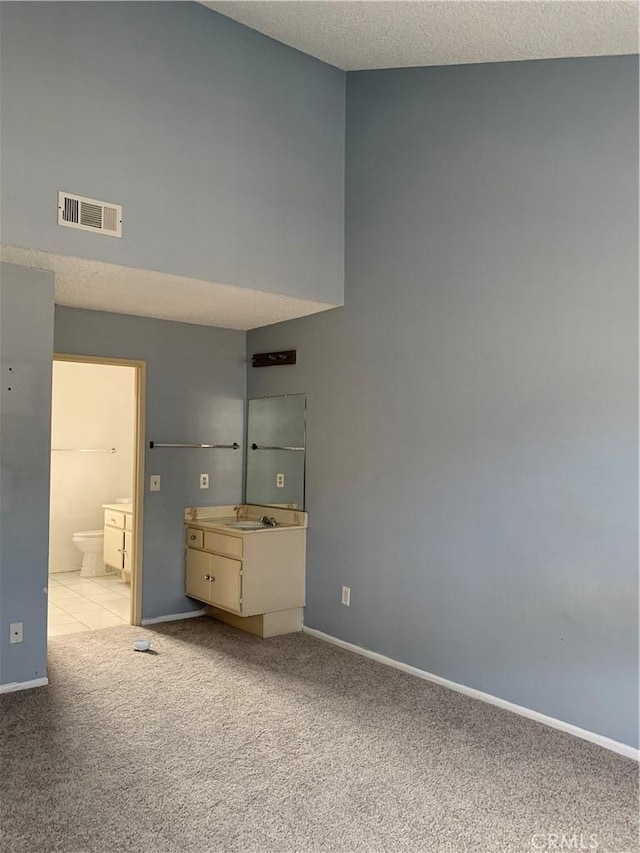 unfurnished bedroom featuring baseboards, visible vents, light colored carpet, ensuite bath, and a textured ceiling