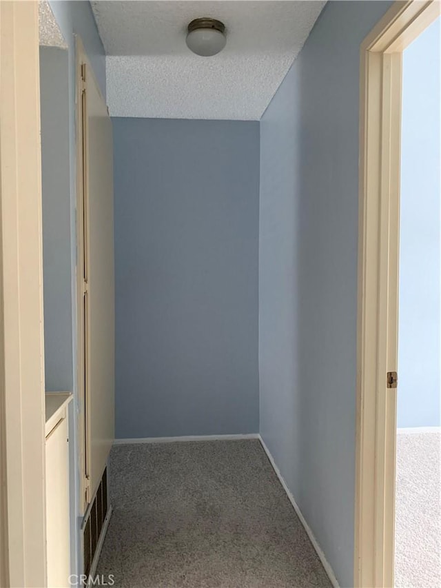 corridor featuring a textured ceiling, carpet, visible vents, and baseboards