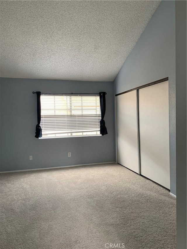 unfurnished bedroom with lofted ceiling, carpet floors, a closet, and a textured ceiling