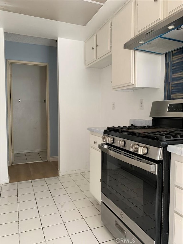 kitchen with white cabinets, gas stove, light countertops, under cabinet range hood, and light tile patterned flooring