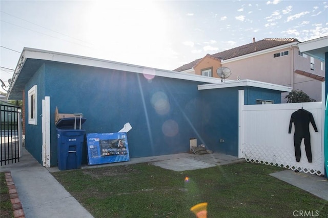 view of home's exterior with a gate, fence, a lawn, and stucco siding