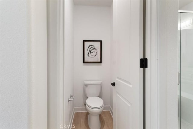 bathroom featuring a stall shower, toilet, baseboards, and wood finished floors