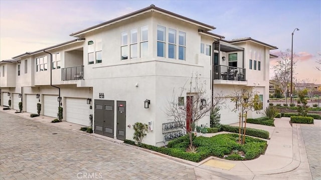 view of front of property with stucco siding, an attached garage, driveway, and a balcony