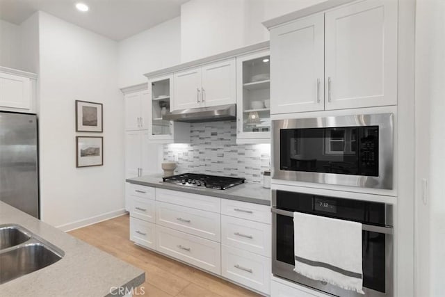 kitchen featuring under cabinet range hood, tasteful backsplash, stainless steel appliances, light wood-style floors, and white cabinets