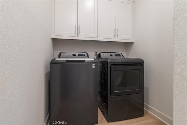 clothes washing area with washer and dryer, baseboards, cabinet space, and light wood-type flooring