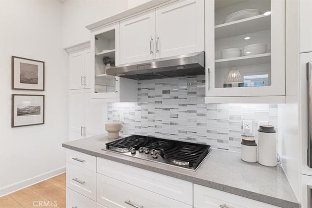 kitchen featuring tasteful backsplash, glass insert cabinets, under cabinet range hood, light wood-style floors, and stainless steel gas stovetop