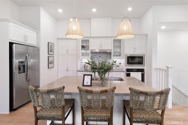 kitchen with light wood-style flooring, under cabinet range hood, appliances with stainless steel finishes, white cabinets, and decorative backsplash