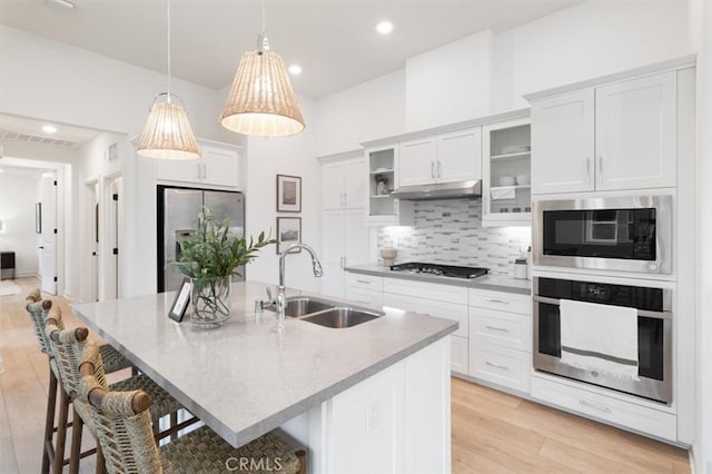 kitchen featuring under cabinet range hood, a breakfast bar area, decorative backsplash, stainless steel appliances, and a sink