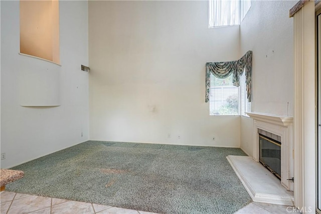 unfurnished living room featuring light colored carpet, a towering ceiling, and a glass covered fireplace