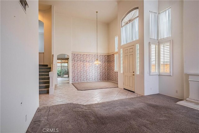 tiled entryway featuring arched walkways, carpet, and a towering ceiling