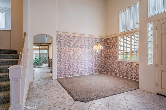 foyer entrance with stairs, a towering ceiling, light carpet, wallpapered walls, and arched walkways