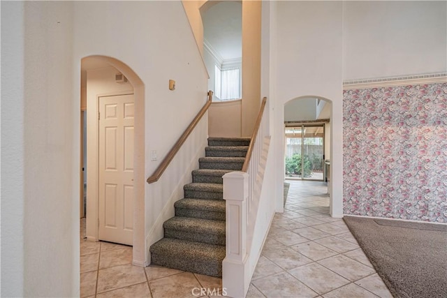 staircase with arched walkways, tile patterned flooring, wallpapered walls, and a towering ceiling