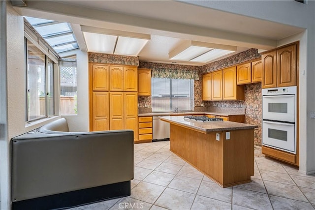 kitchen with brown cabinetry, a kitchen island, tasteful backsplash, light tile patterned floors, and stainless steel appliances