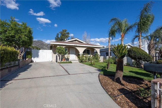 ranch-style home featuring a gate, fence, a mountain view, a front lawn, and stucco siding