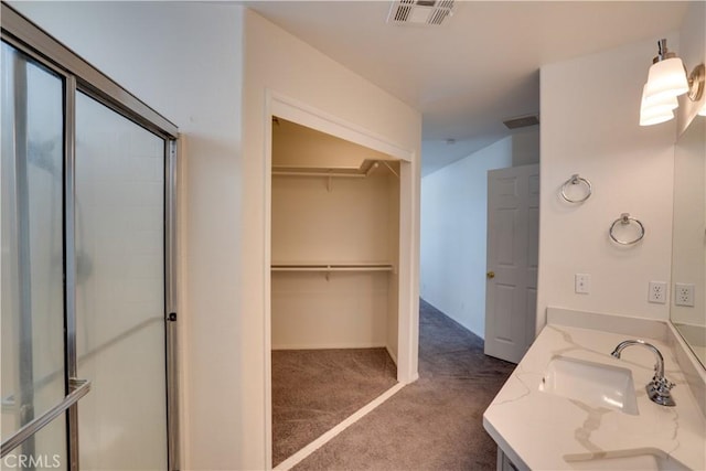 full bathroom featuring double vanity, visible vents, an enclosed shower, a walk in closet, and a sink