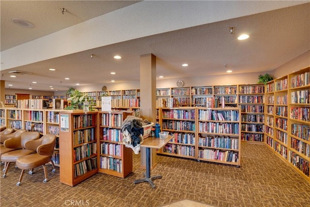 living area with a textured ceiling, wall of books, and carpet flooring