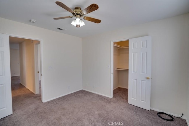 unfurnished bedroom featuring a walk in closet, carpet, visible vents, a ceiling fan, and baseboards