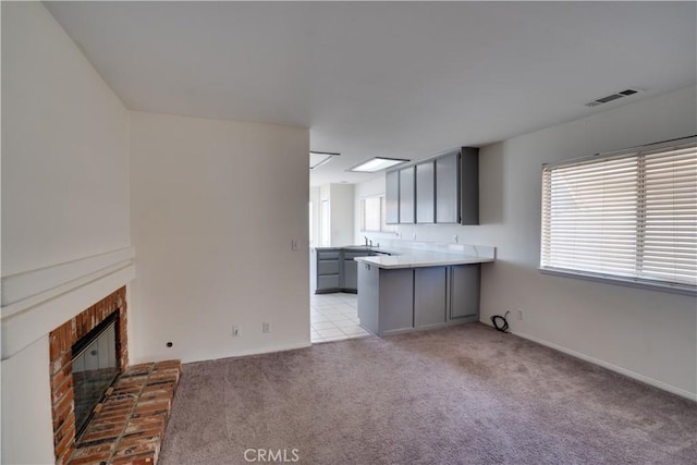 kitchen with a fireplace, gray cabinets, visible vents, light carpet, and a peninsula