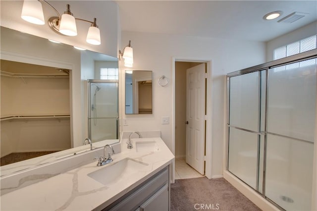 full bathroom featuring a stall shower, a walk in closet, visible vents, and a sink