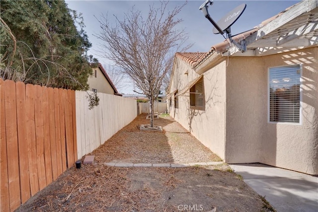 view of side of home with a tile roof, fence, and stucco siding