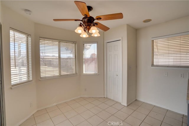 interior space featuring a closet, light tile patterned flooring, a ceiling fan, and baseboards