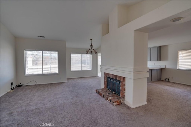 unfurnished living room with visible vents, a fireplace, an inviting chandelier, and light colored carpet