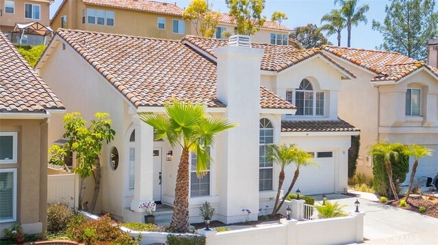 mediterranean / spanish home featuring a garage, fence, driveway, stucco siding, and a chimney