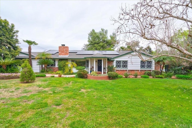 ranch-style house with a chimney, a front lawn, solar panels, and brick siding