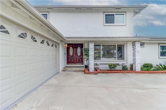 entrance to property featuring a garage, driveway, and stucco siding