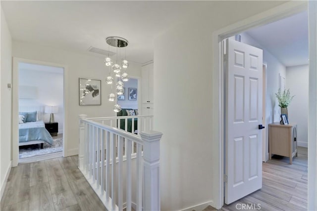 corridor with light wood finished floors, an inviting chandelier, an upstairs landing, and baseboards