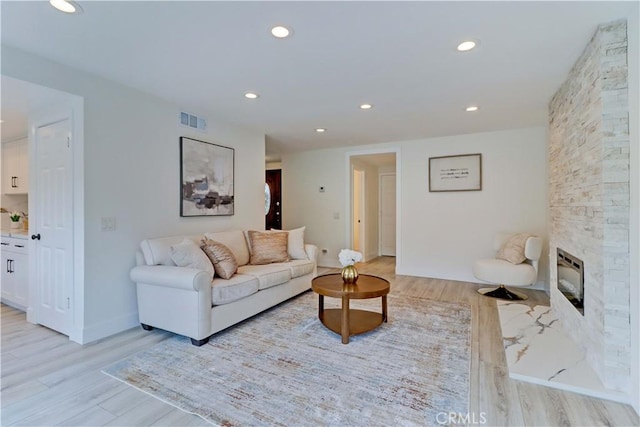 living room featuring light wood-style floors, recessed lighting, visible vents, and a stone fireplace