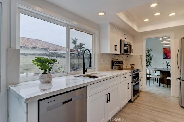 kitchen with light stone counters, appliances with stainless steel finishes, white cabinetry, a sink, and light wood-type flooring