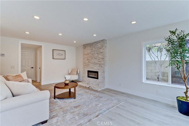 living room featuring light wood-style flooring, baseboards, a stone fireplace, and recessed lighting