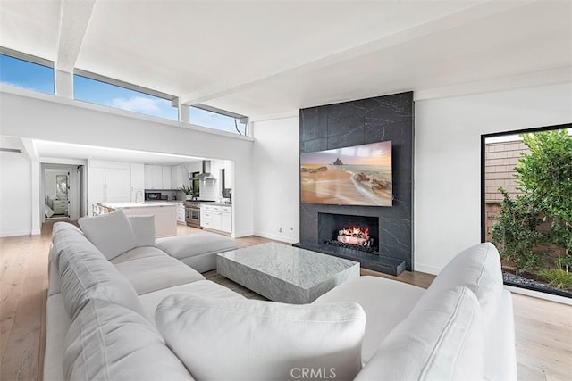 living room with light wood-type flooring, beamed ceiling, baseboards, and a premium fireplace