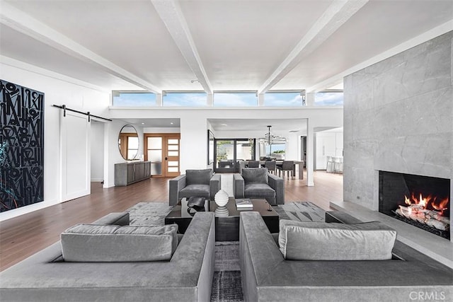 living area with a barn door, a tile fireplace, wood finished floors, french doors, and beam ceiling