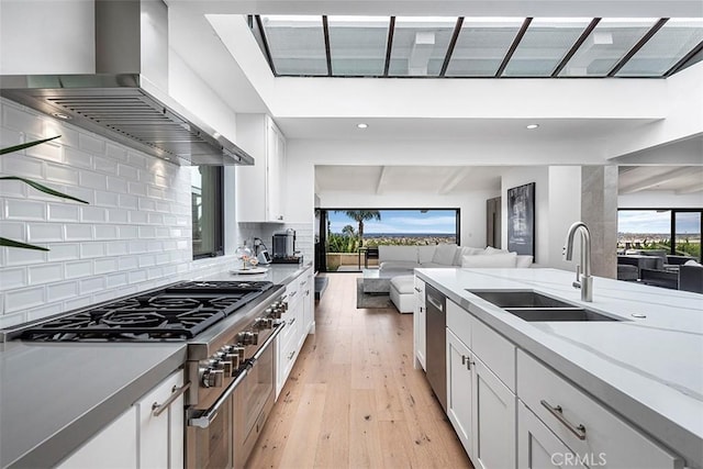 kitchen with tasteful backsplash, wall chimney exhaust hood, appliances with stainless steel finishes, open floor plan, and a sink