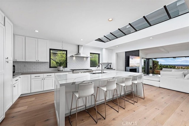 kitchen with tasteful backsplash, light wood-type flooring, a sink, and wall chimney range hood
