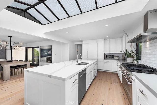kitchen featuring light wood finished floors, tasteful backsplash, appliances with stainless steel finishes, wall chimney range hood, and a sink