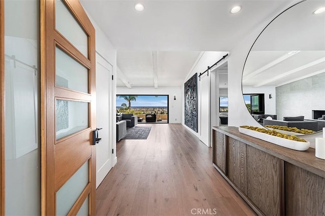 corridor featuring light wood finished floors, a barn door, beamed ceiling, and recessed lighting