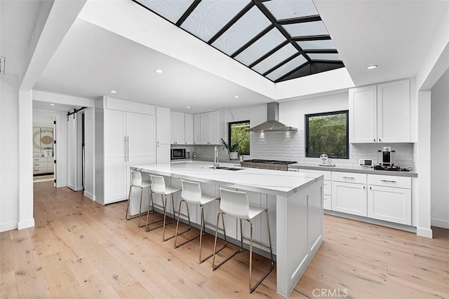 kitchen featuring white cabinetry, light wood finished floors, wall chimney exhaust hood, and a barn door