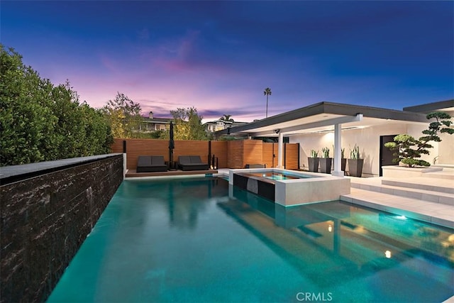 pool at dusk featuring a pool with connected hot tub, fence, and a patio