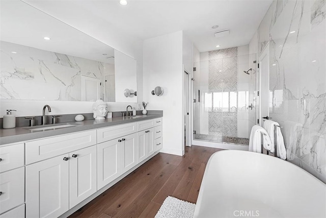 bathroom with double vanity, wood finished floors, a sink, and a shower stall