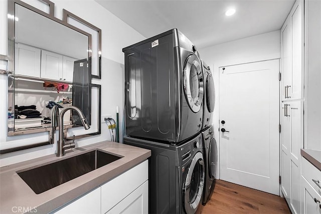 clothes washing area with wood finished floors, recessed lighting, a sink, and stacked washer / drying machine