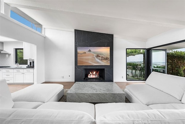 living area featuring light wood finished floors, plenty of natural light, beam ceiling, and a high end fireplace
