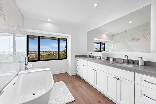 full bathroom featuring double vanity, a freestanding tub, a sink, and wood finished floors