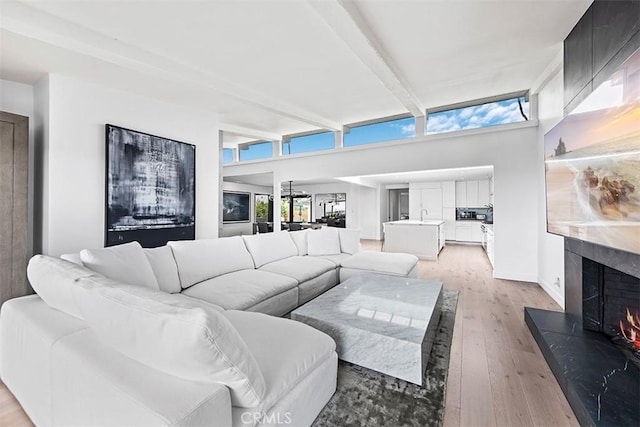 living area with light wood-type flooring, a fireplace, and beamed ceiling