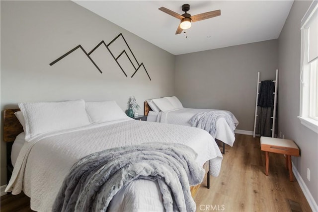 bedroom with a ceiling fan, wood finished floors, visible vents, and baseboards