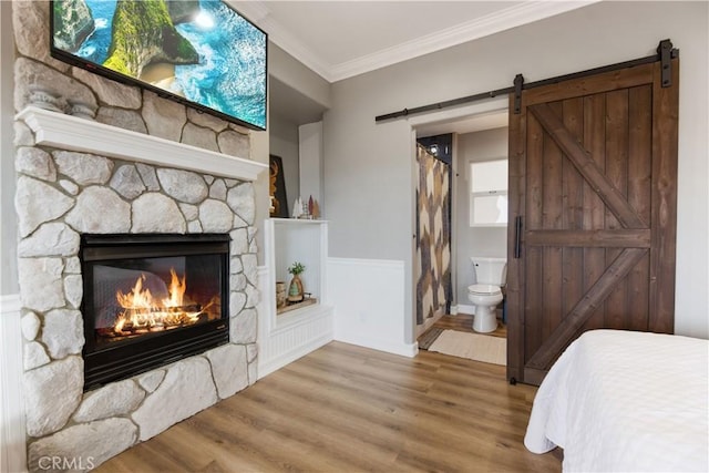 bedroom with a stone fireplace, a barn door, connected bathroom, wood finished floors, and crown molding