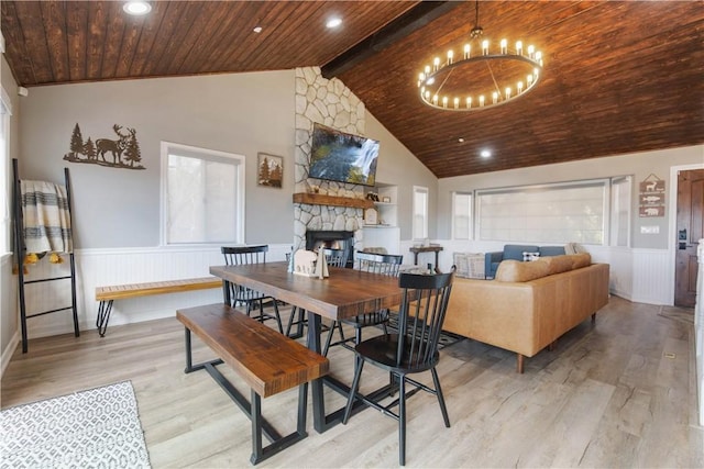 dining room featuring wood ceiling, a chandelier, a stone fireplace, and wainscoting