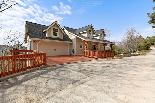 view of front of house featuring roof with shingles, driveway, a deck, and an attached garage